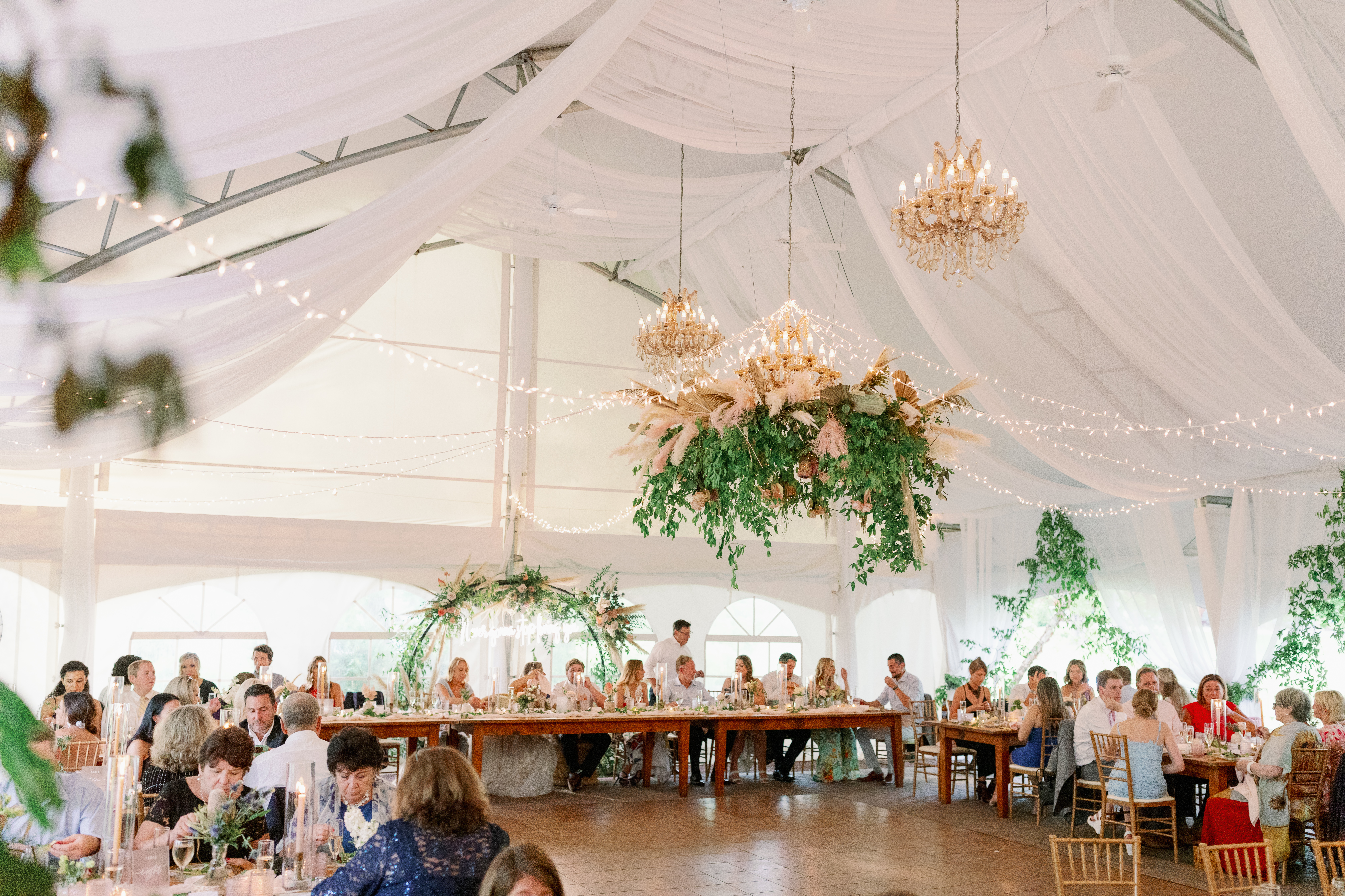 big tent with bridal party seated at the top of the tent, guests seated at tables surrounding the dance floor